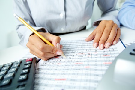 Photo of human hands holding pencil and marking numbers in documents