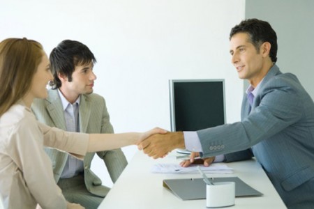 Young couple sitting across desk from businessman, woman shaking hands with businessman, side view
